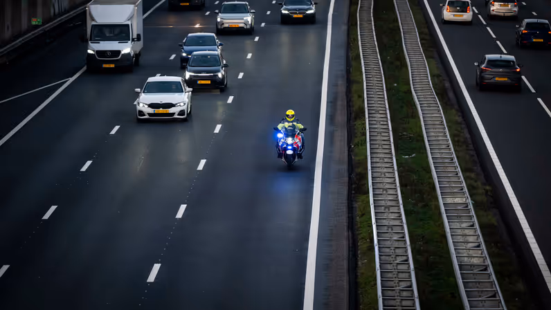Een motorbegeleider van de Koninklijke Marechaussee rijdt met zwaailicht over de snelweg terwijl het overige verkeer ruimte maakt.