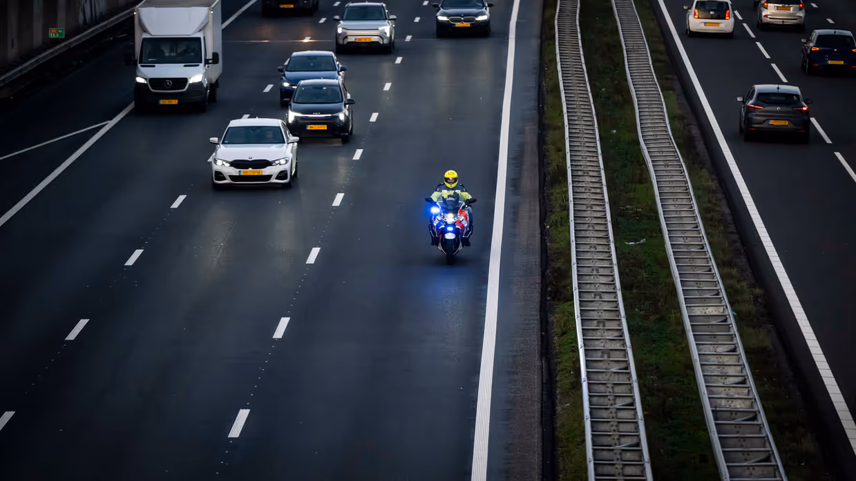 Een motorbegeleider van de Koninklijke Marechaussee rijdt met zwaailicht over de snelweg terwijl het overige verkeer ruimte maakt.
