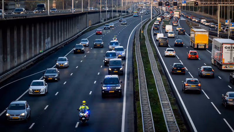 Een motorbegeleider van de Koninklijke Marechaussee rijdt voor een colonne dienstvoertuigen over de snelweg.