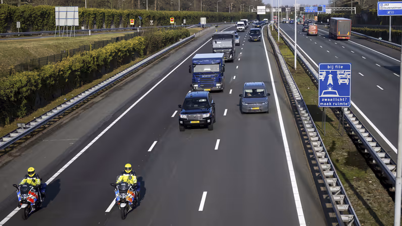 Motorbegeleiders van de Koninklijke Marechaussee rijden voor een colonne dienstvoertuigen over de snelweg.
