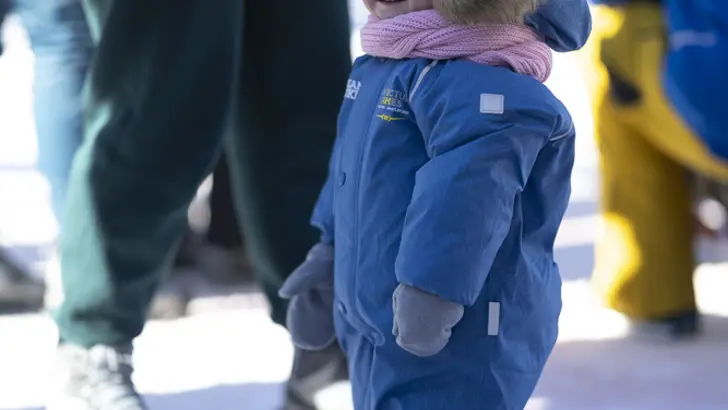 Een kindje met skipak en wollen muts kijkt naar de camera.