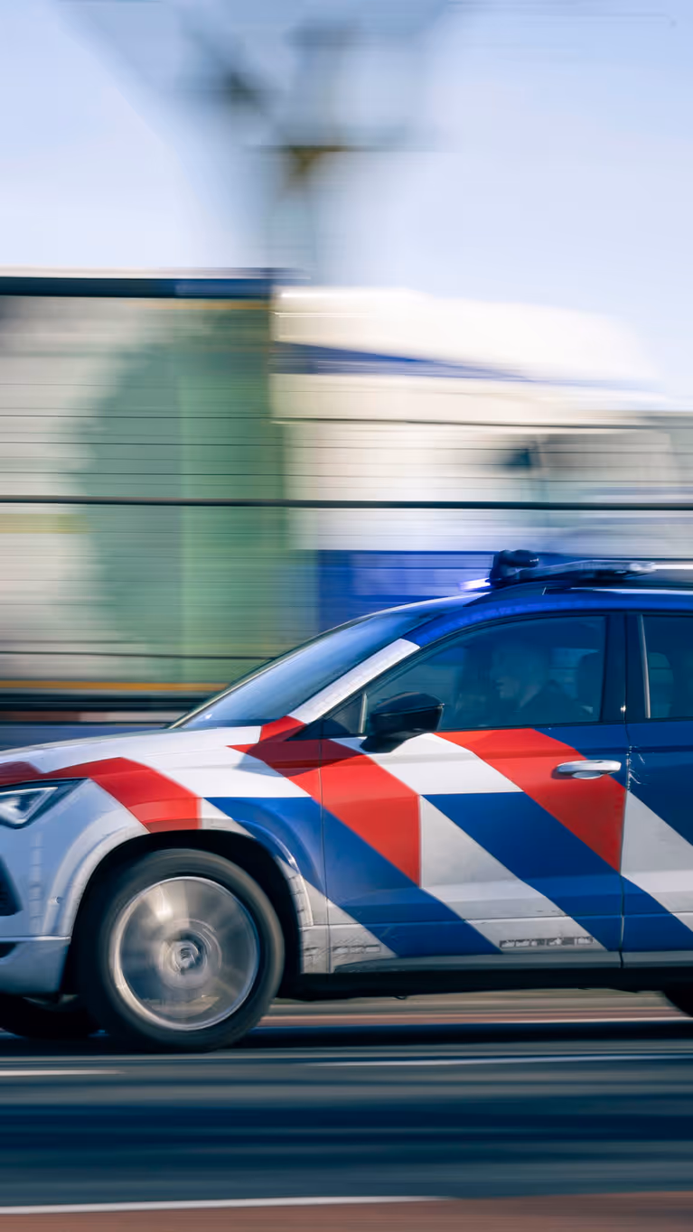 Een dienstvoertuig met zwaailicht dat snel langs een vangrail rijdt.