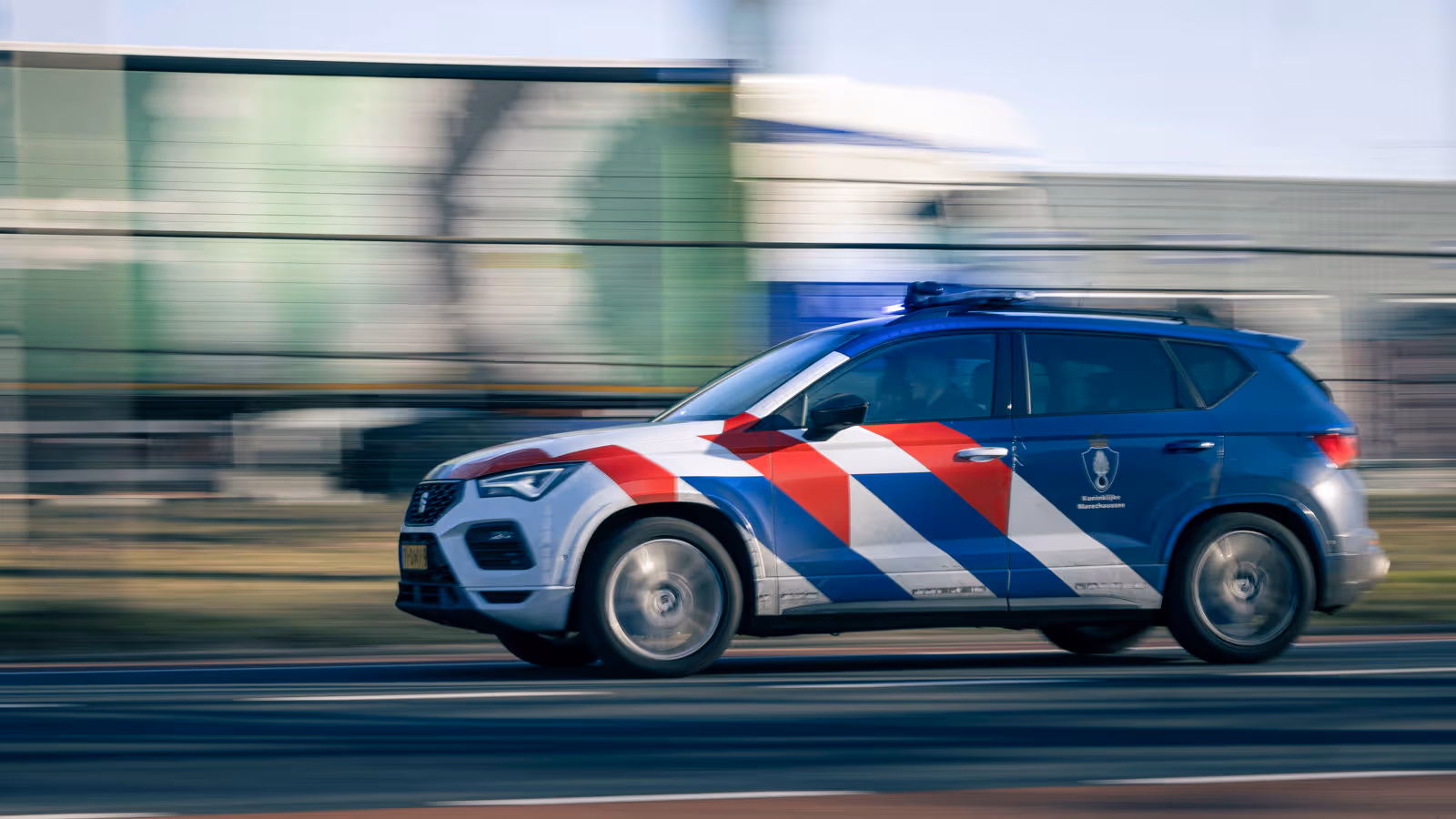 Een dienstvoertuig met zwaailicht dat snel langs een vangrail rijdt.