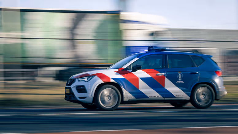 Een dienstvoertuig met zwaailicht dat snel langs een vangrail rijdt.
