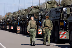 Rij militaire voertuigen. Daarnaast lopen 2 militairen.