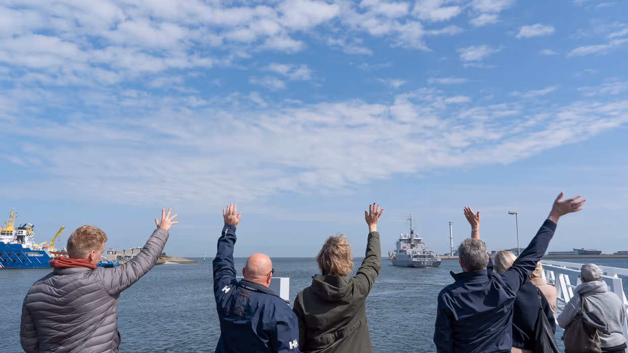 Mensen zwaaien vanaf de kade een marineschip uit.