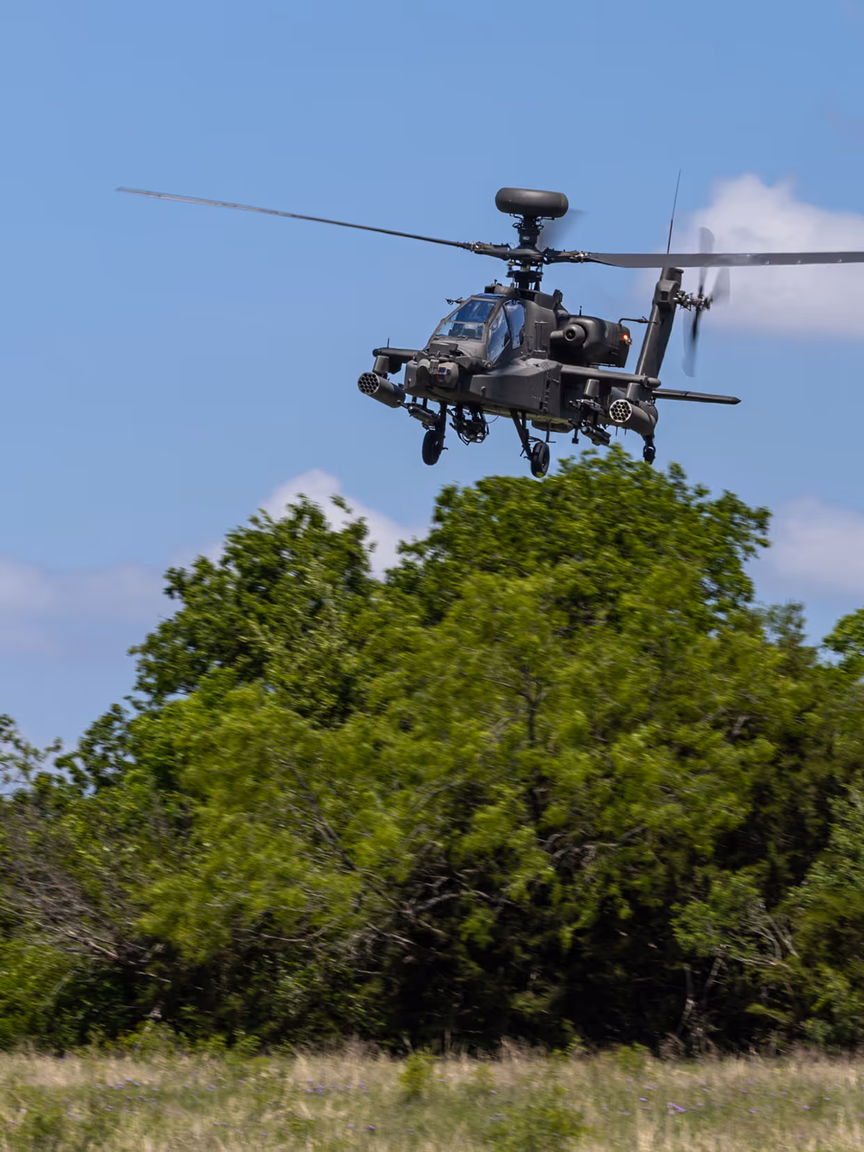 Een laagvliegende Apache boven hoge struiken en gras.
