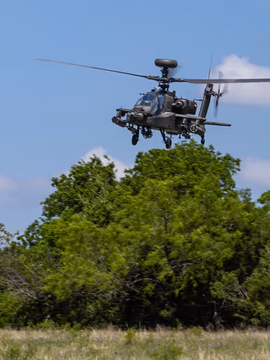 Een laagvliegende Apache boven hoge struiken en gras.