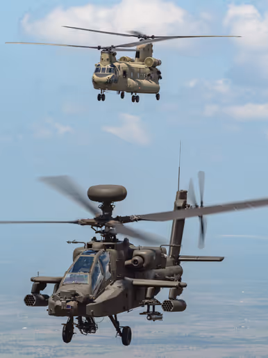 Een vliegende Chinook en Apache tegen een blauwe lucht met een enkel wolkje.