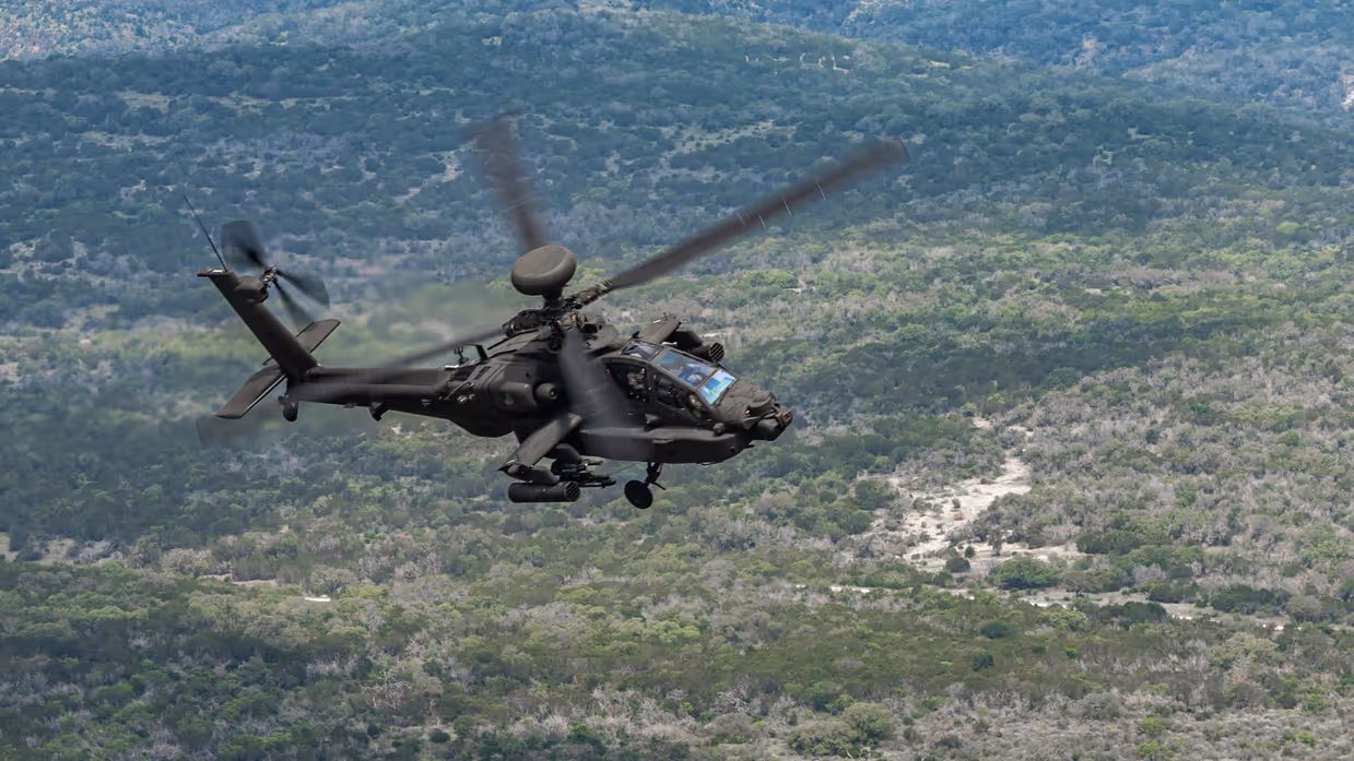 Een Apache vliegend boven begroeide heuvels.