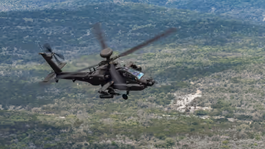 Een Apache vliegend boven begroeide heuvels.