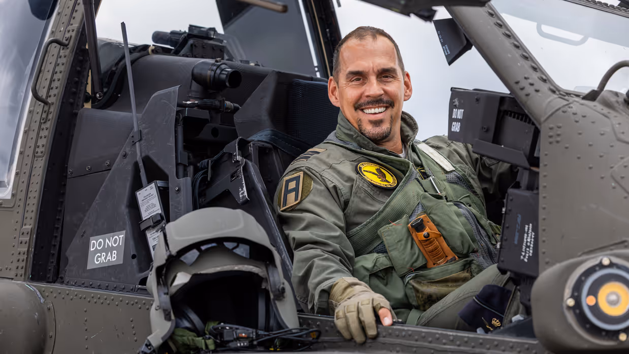 Luitenant-kolonel Wilko de Waard kijkt lachend de camera in vanuit de cockpit van een Apache. Zijn helm ligt naast hem op het airframe.