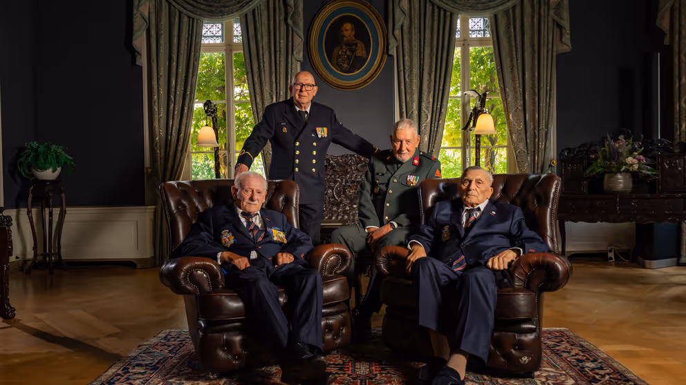 4 veteranen poseren, 2 van hen zitten in een stoel.