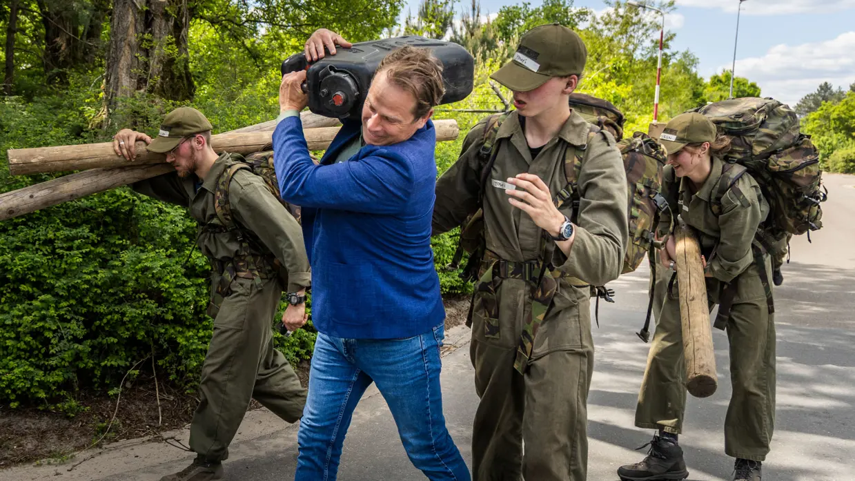 Tuinman in blauw jasje sjouwt een grote jerrycan op zijn schouders. 