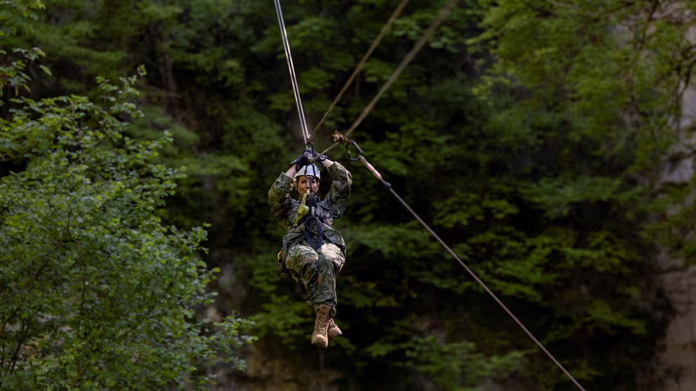 Militair daalt tussen de bomen af met een zipline.