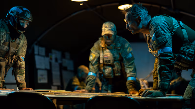 Een groep van drie militairen buigt over een kaart op tafel en overlegt.