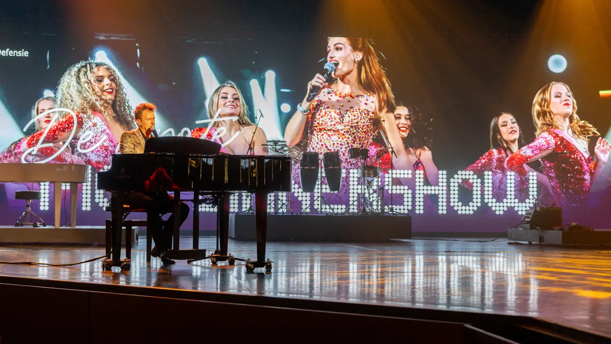 Alt: Links een zanger achter een piano. Rechts een soort toren met daarop smakelijke hapjes. 