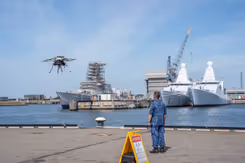 Militair staat op kade en kijkt naar drone die opstijgt.