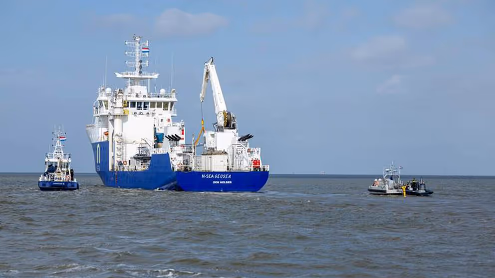 Het schip de NS Geosea, van de onderkant blauw en de bovenkant wit, vaart op zee. Links en rechts een klein bootje.
