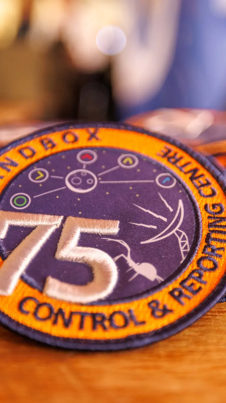 Een verzameling oranje-paarse badges met daarop het getal 75 en de teksten Bandbox en Control & Reporting Centre.