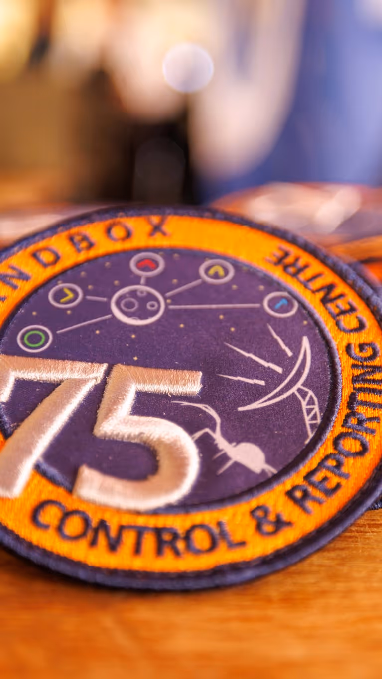 Een verzameling oranje-paarse badges met daarop het getal 75 en de teksten Bandbox en Control & Reporting Centre.