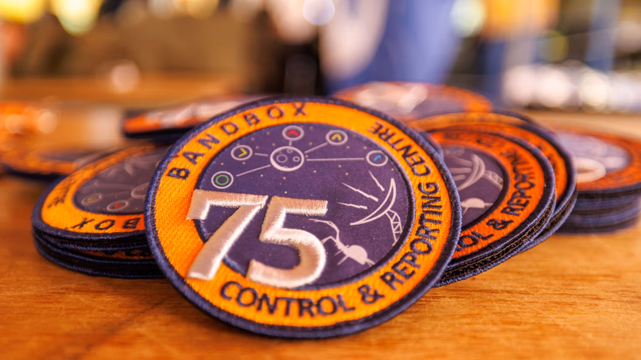 Een verzameling oranje-paarse badges met daarop het getal 75 en de teksten Bandbox en Control & Reporting Centre.