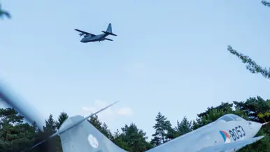 Een Italiaanse C-130 vliegt over een F-104G Starfighter die op de grond staat.  