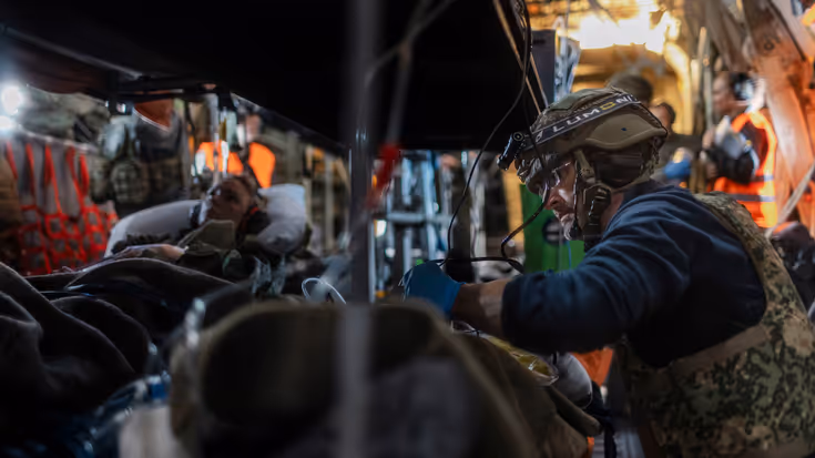 Twee gewonde militairen op brancards in een helikopter. Een militair medicus behandelt een van de twee.