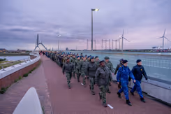 Militairen lopen over een brug, vrouwen voorop.