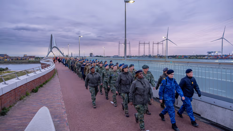 Militairen lopen over een brug, vrouwen voorop.