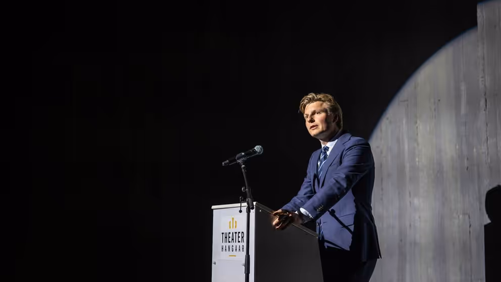 Minister Ruben Brekelmans tegen donkere achtergrond achter katheder.