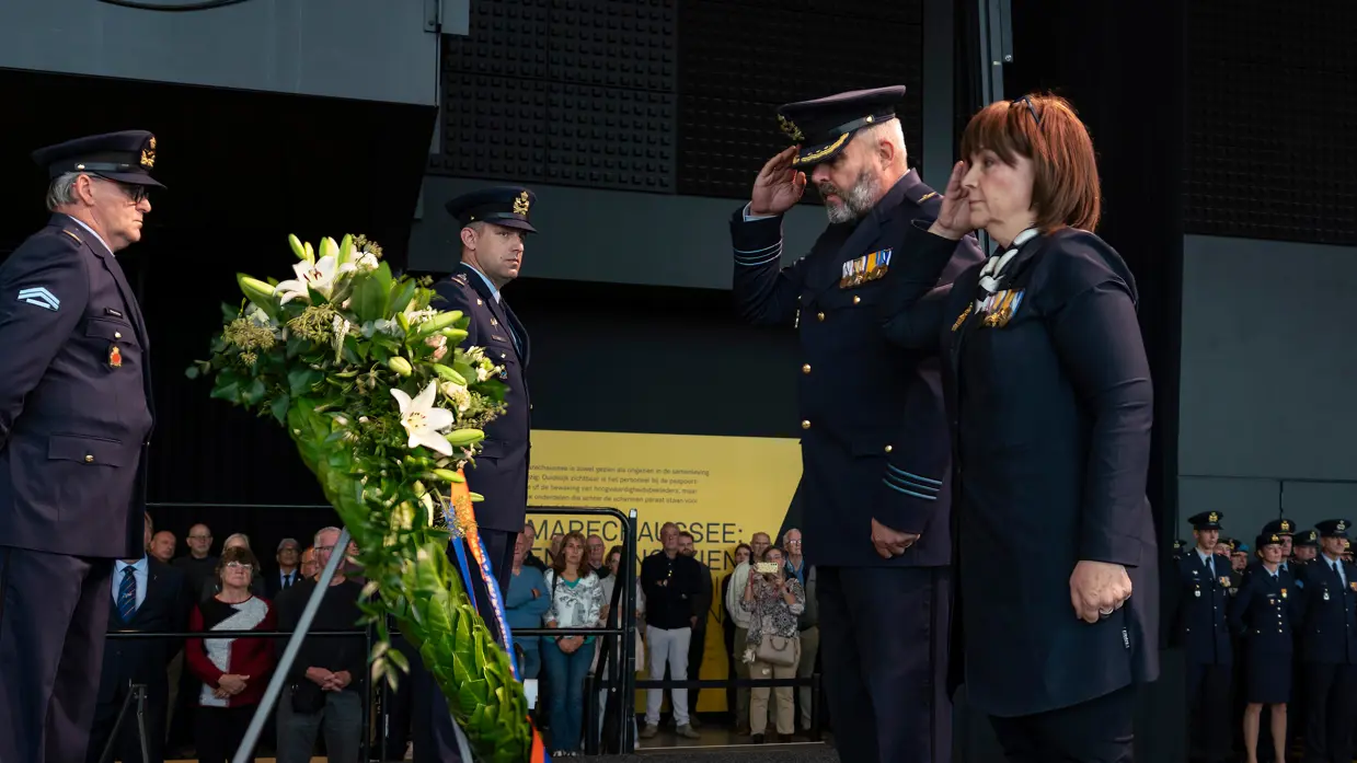 Een vrouw en een militair brengen een eregroet aan een krans. Daar omheen staan nog twee militairen.