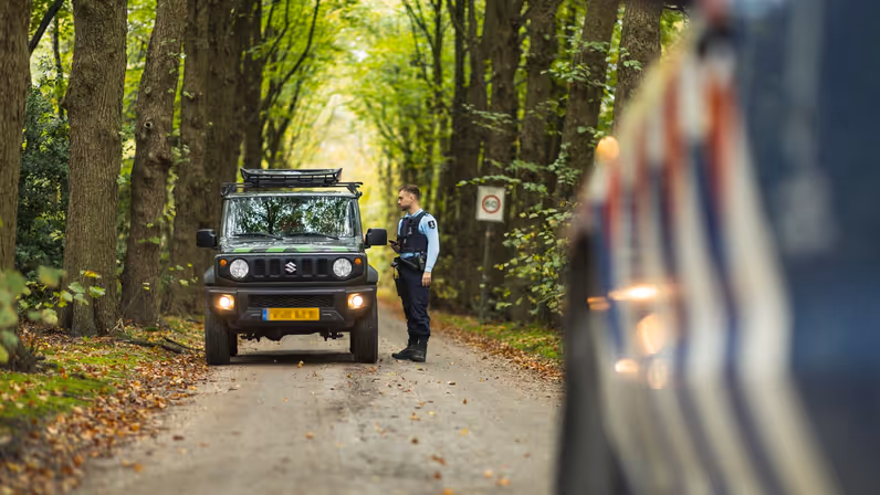 Wachtmeester Joris spreekt met een bestuurder in een bosgebied op de Veluwe.