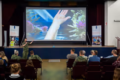Spreker traumachirurg kolonel Vincent Stirler wijst naar een afbeelding op een scherm van een spalk die een patient om de pols heeft.