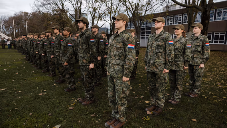 Militairen staan opgesteld. Ze dragen een groen pak en een veldpet.