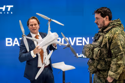 Staatssecretaris Gijs Tuinman op de beursvloer met een drone in zijn hand. Een militair naast hem in uniform. 