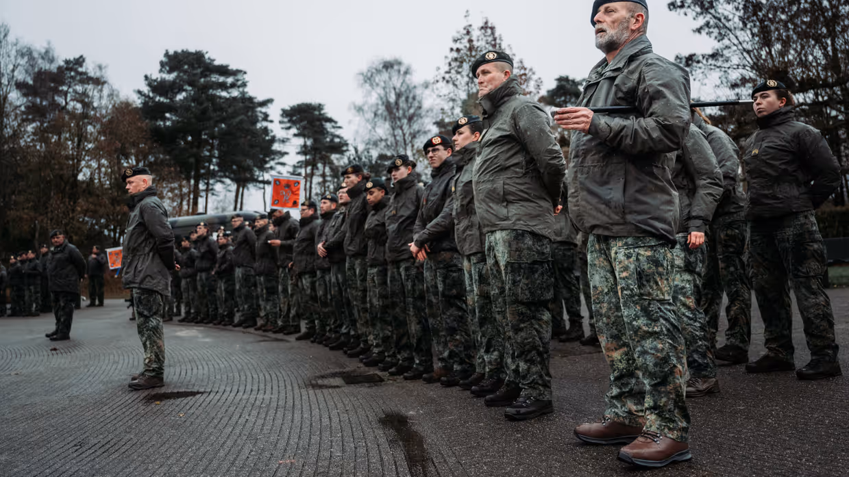 Een peloton militairen staat in rijen geformeerd met daarvoor twee andere militairen.