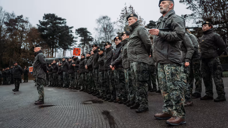 Een peloton militairen staat in rijen geformeerd met daarvoor twee andere militairen.