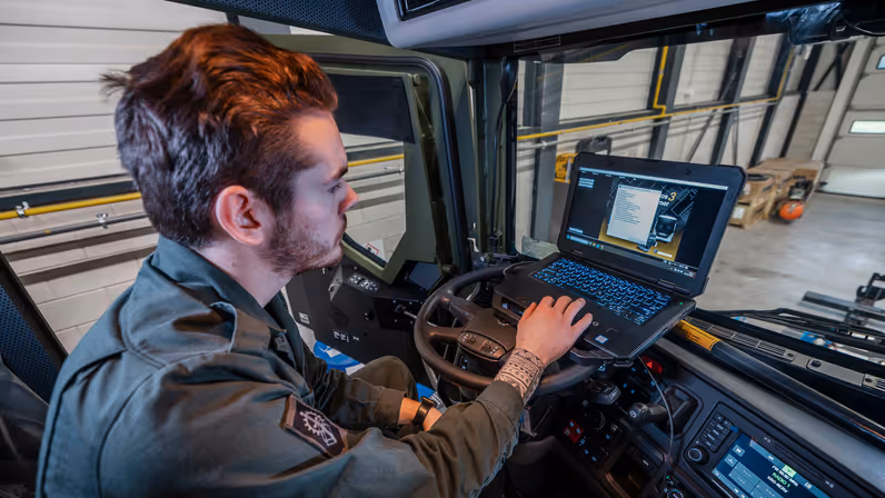 Monteur zit in cabine met laptop op stuur om software voertuig te testen.