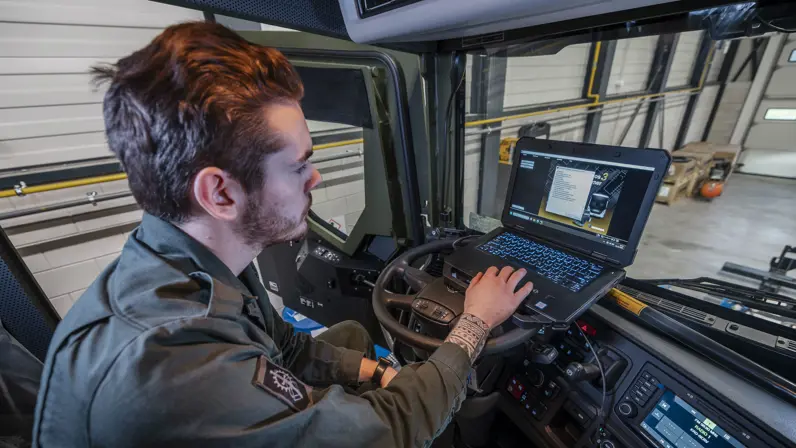 Monteur zit in cabine met laptop op stuur om software voertuig te testen.