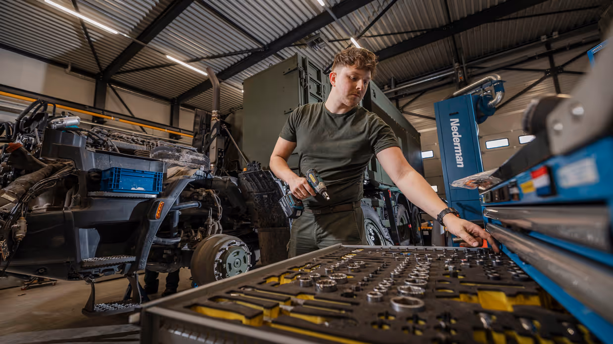 Monteur in werkplaats pakt onderdeel uit gereedschapskast.