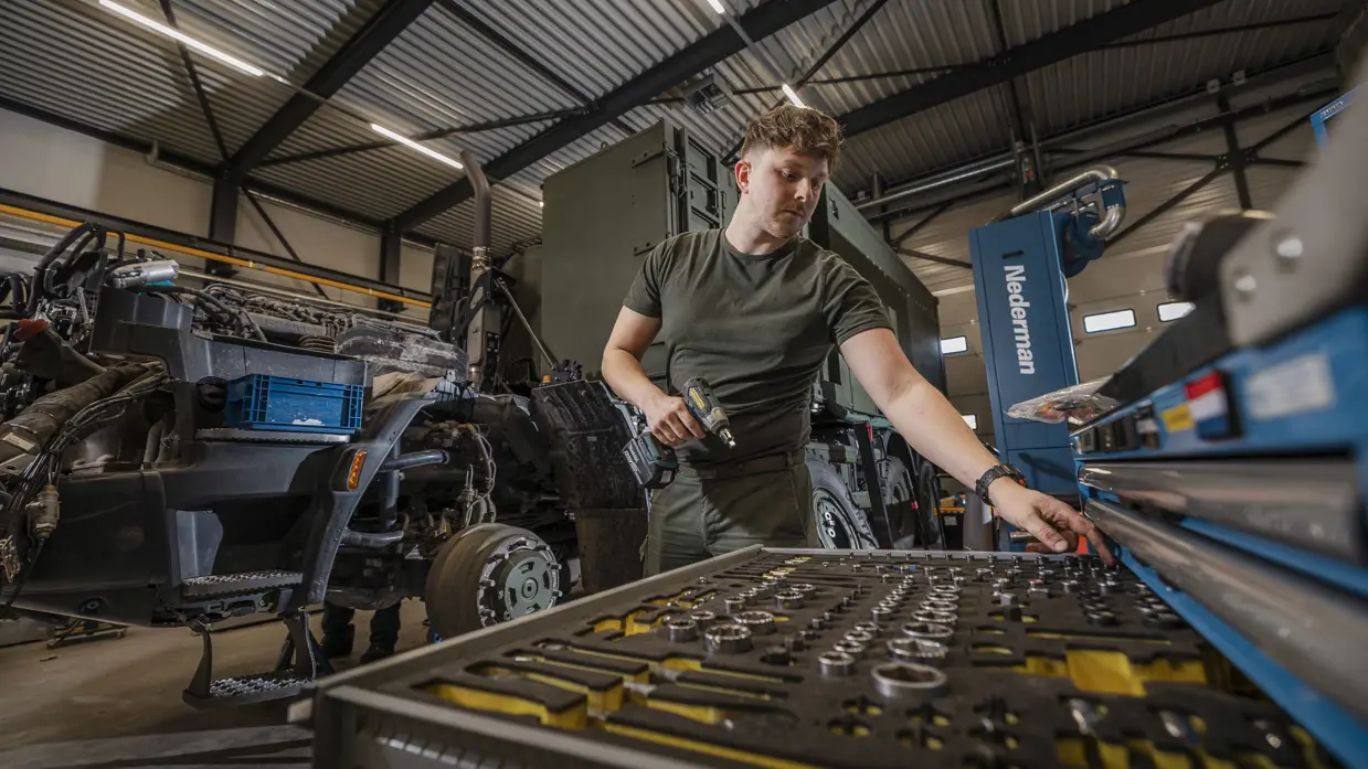 Monteur in werkplaats pakt onderdeel uit gereedschapskast.