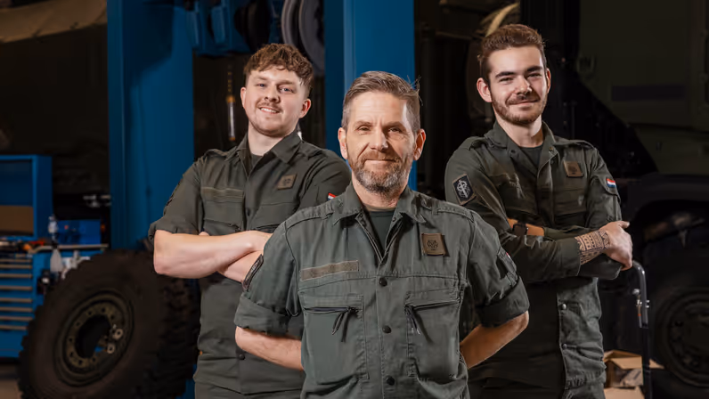 3 monteurs in groene werkkleding staan lachend naast elkaar.