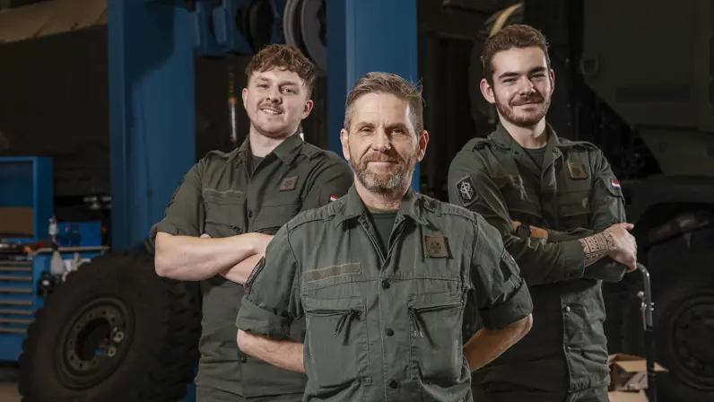 3 monteurs in groene werkkleding staan lachend naast elkaar.