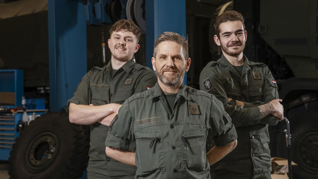 3 monteurs in groene werkkleding staan lachend naast elkaar.