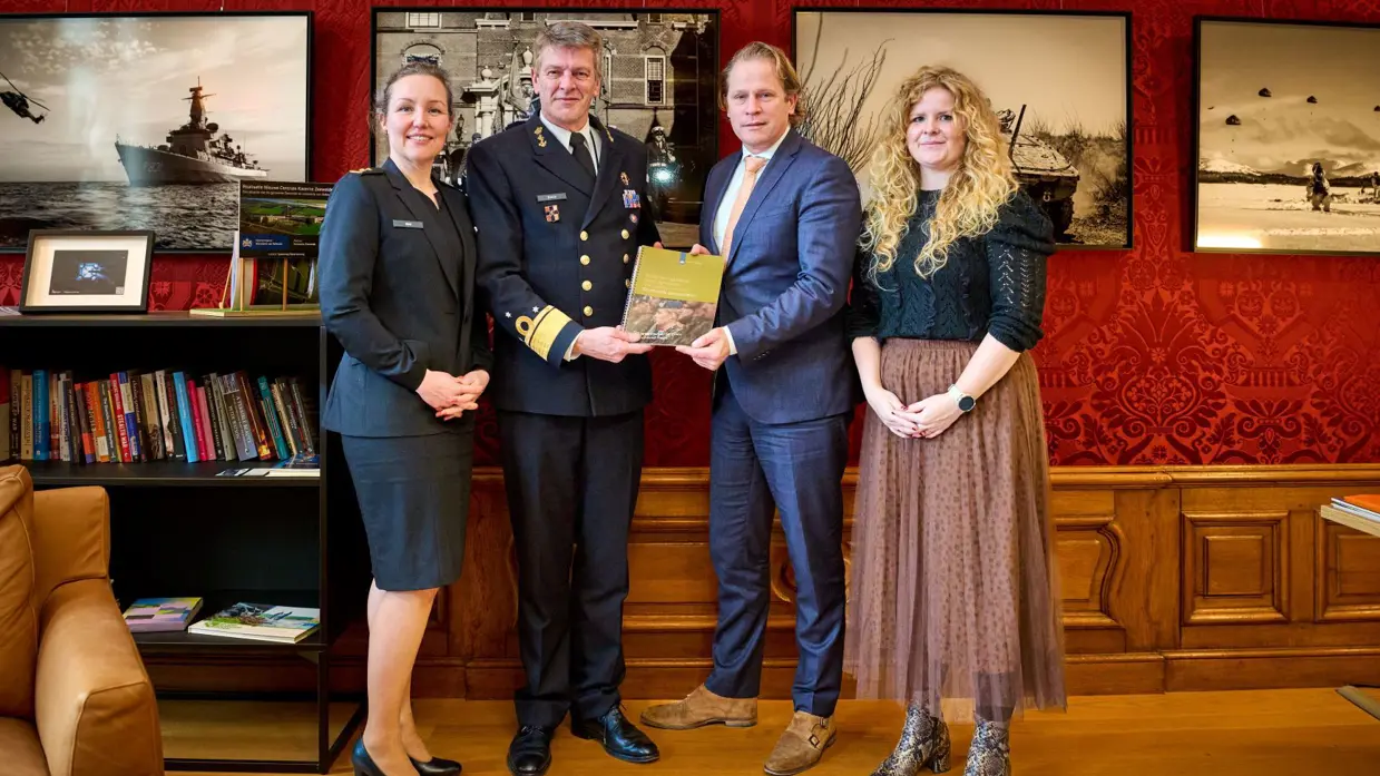 Vier staande personen in een kleine ruimte, waaronder Inspecteur-Generaal der Krijgsmacht viceadmiraal Boudewijn Boots met het themarapport van 2025.
