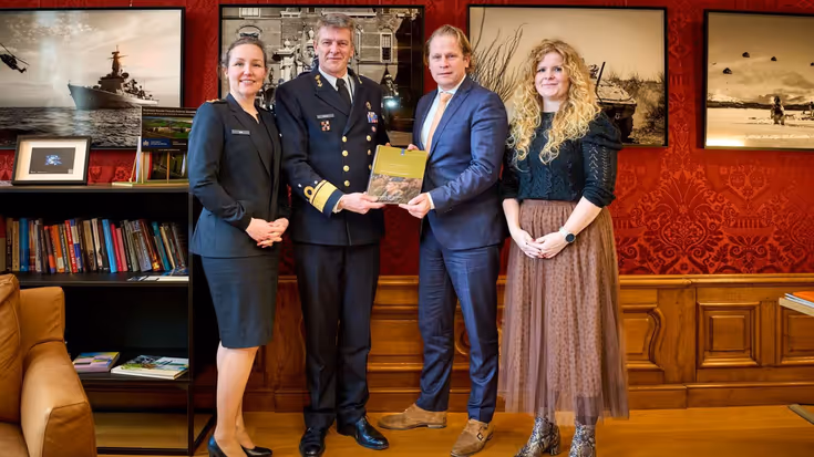 Vier staande personen in een kleine ruimte, waaronder Inspecteur-Generaal der Krijgsmacht viceadmiraal Boudewijn Boots met het themarapport van 2025.