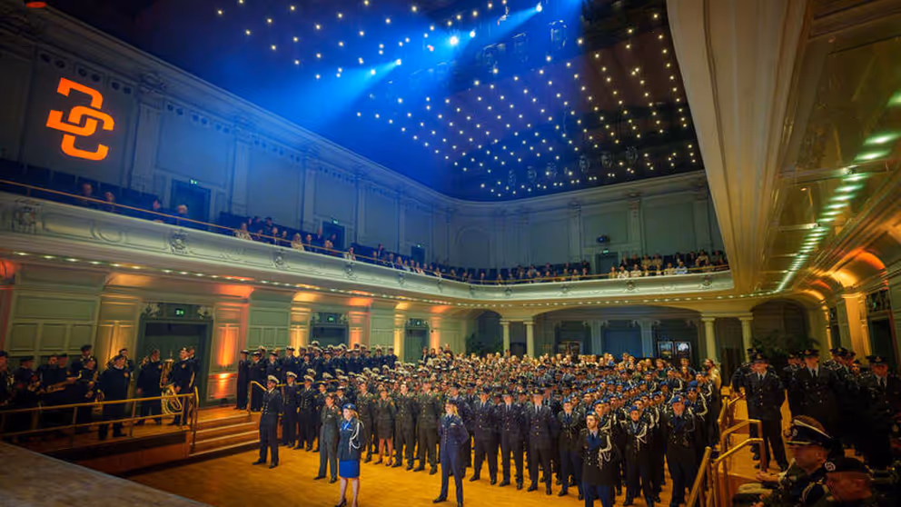 Zaal met honderden militairen die naar het podium staan te kijken.