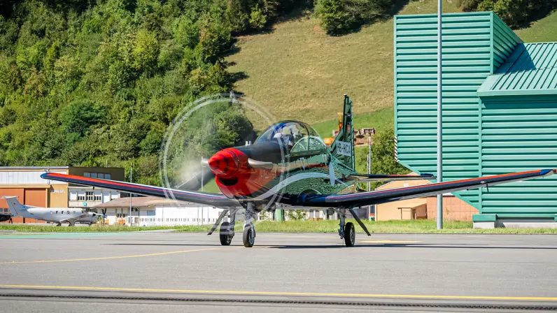 Een PC-7 met draaiende propeller, schuin van voren gezien. In de achtergrond staan nog twee andere vliegtuigen.