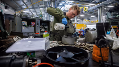 Een monteur druk aan het werk in een grote hal. 